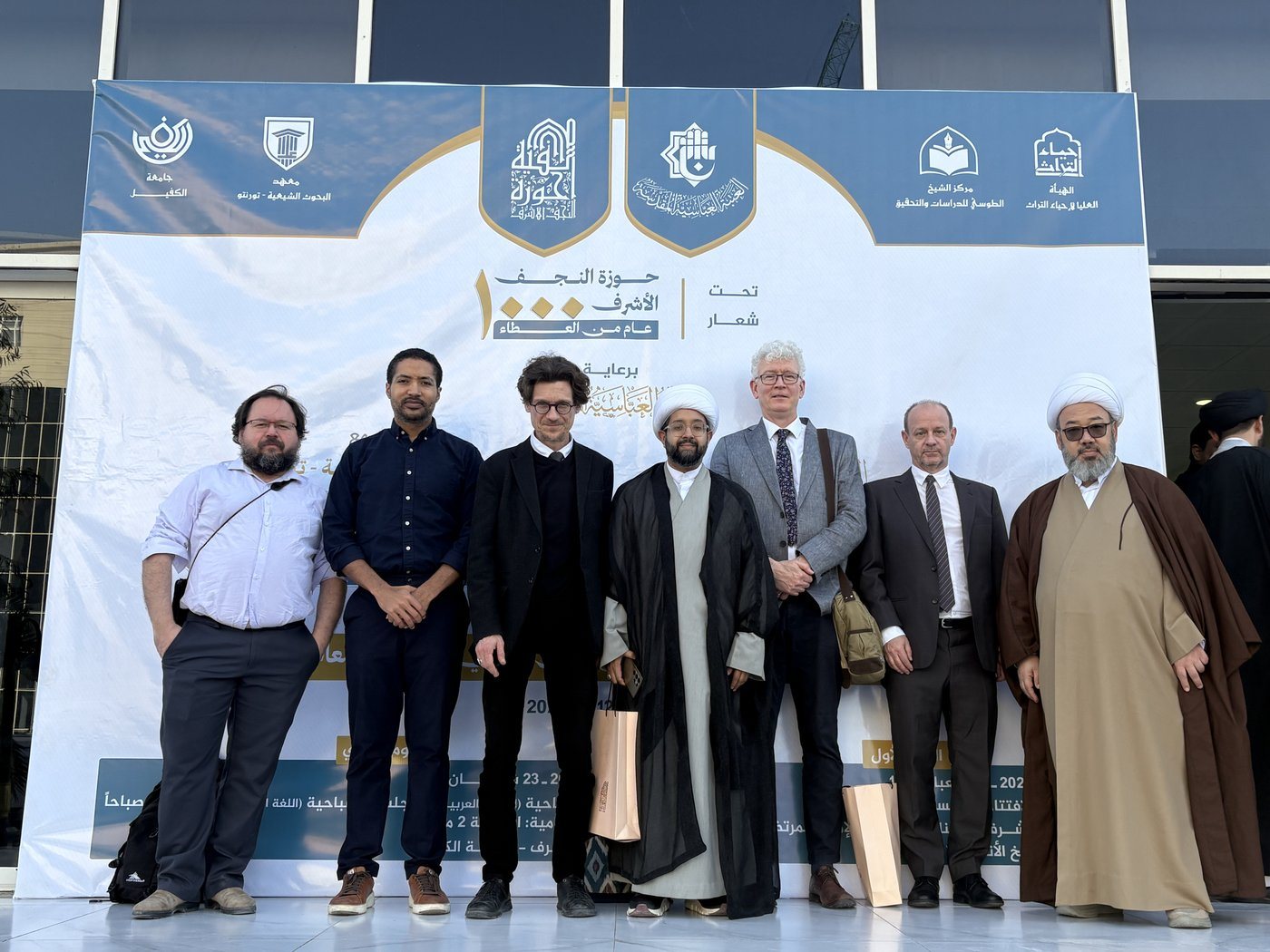 Dr. Hewko with fellow delegates and hosts before the banner marking the Najaf hawza’s thousand-year anniversary.