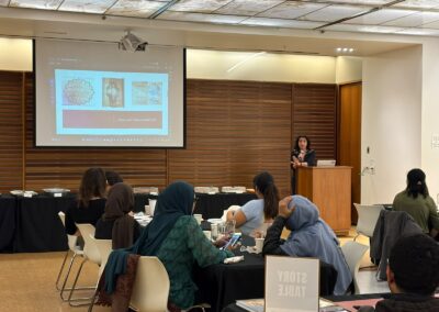 Presenter at the podium discussing manuscript images shown on screen